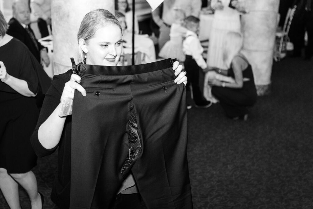 A black and white photo of a woman holding up a pair of mens' dress pants, showing the rear seam, ripped from dancing too hard